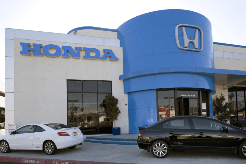 Exterior view of a Honda dealership with two cars parked in front, one white and one black.
